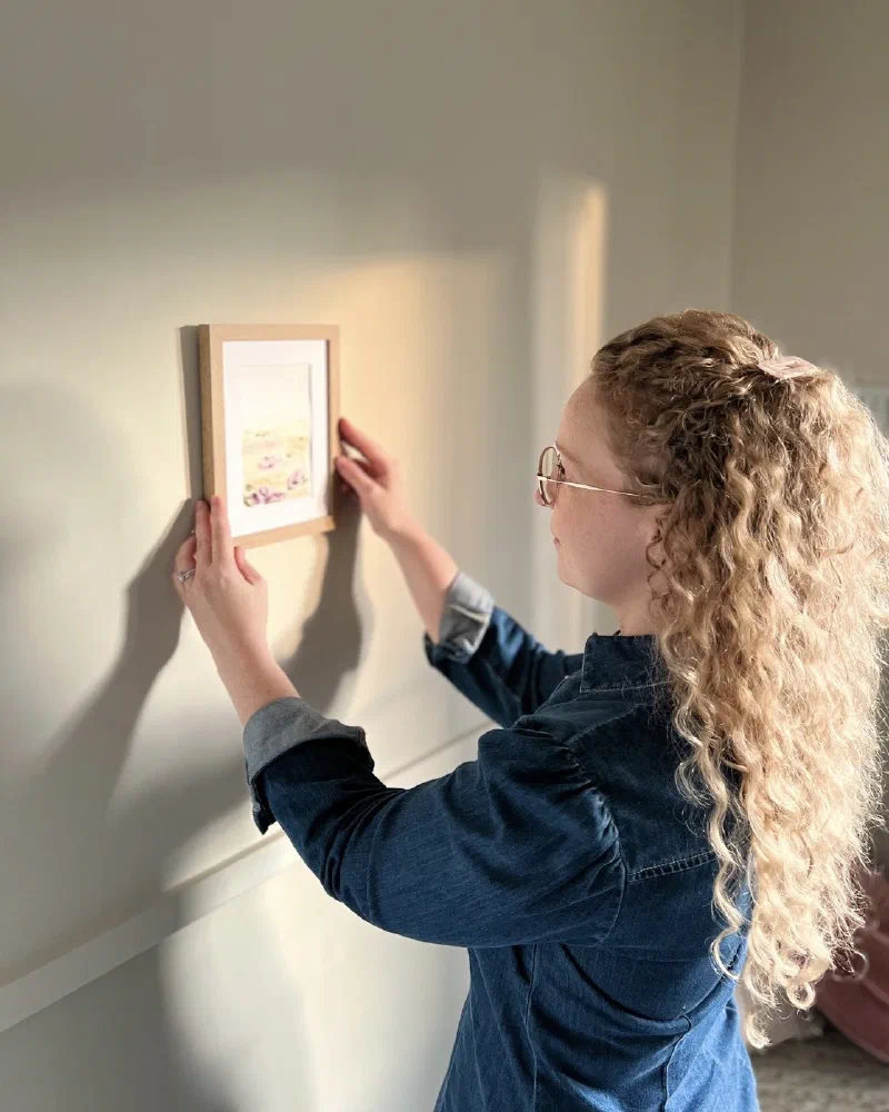 Kezia Richmal hanging a framed painting on a wall